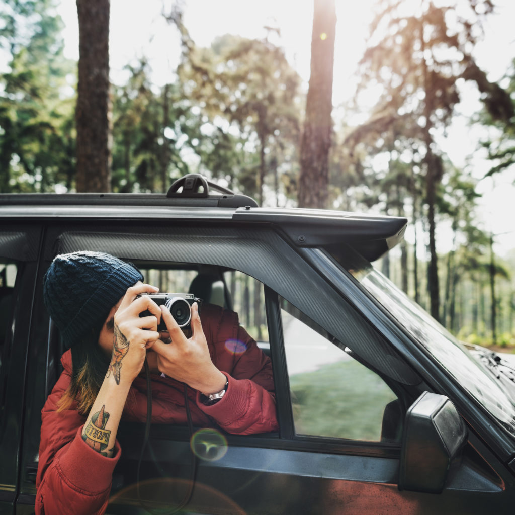 guy taking photos outside of his car while on a road trip