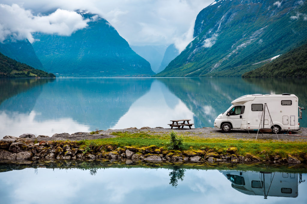 RV parked on lot with scenic lake and mountains in background